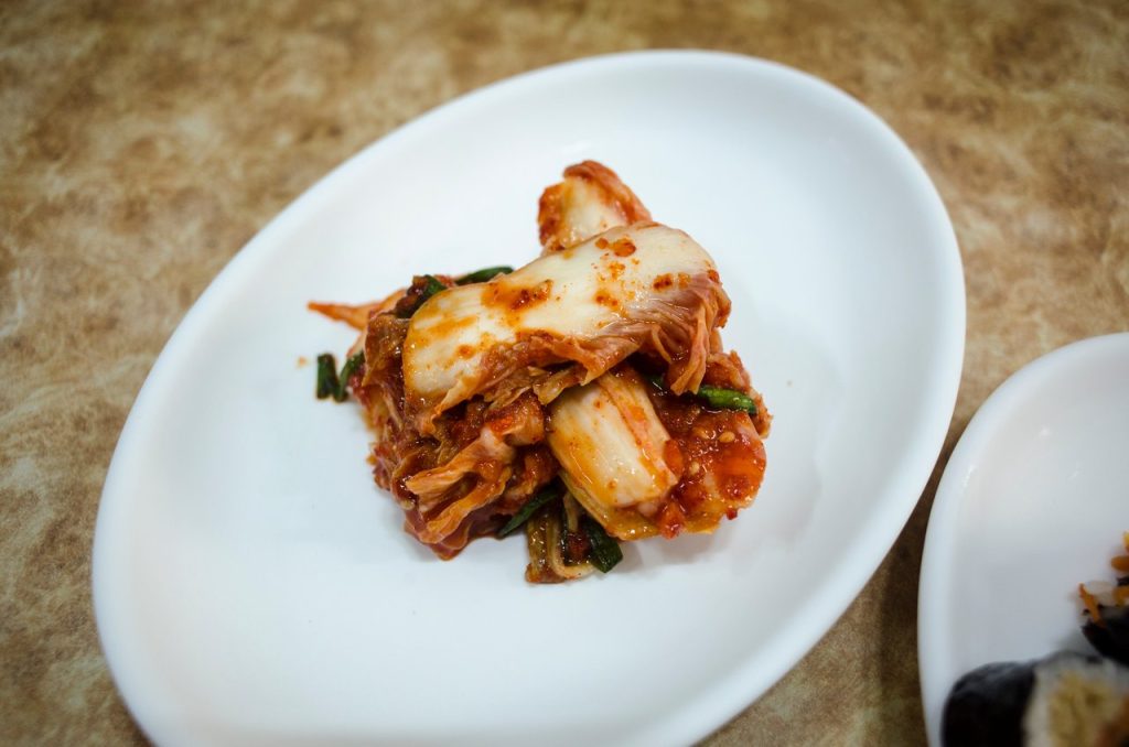 Korean and Western Favourites on Our Menu A plate of traditional fermented Korean kimchi presented elegantly on a white dish.
